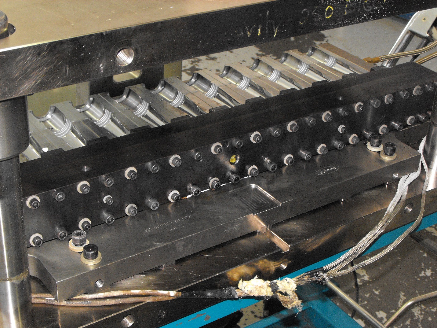 Visão geral de um sistema de moldagem por injeção industrial com coletor e bicos montados em uma placa metálica.